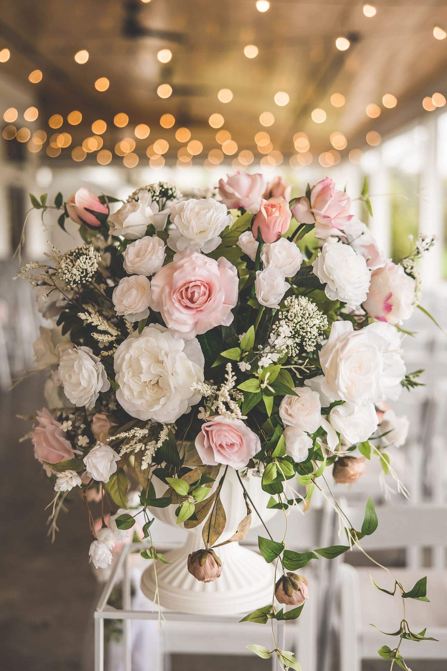A luxurious pink and white rose centerpiece arrangement with baby's breath under warm string lights.