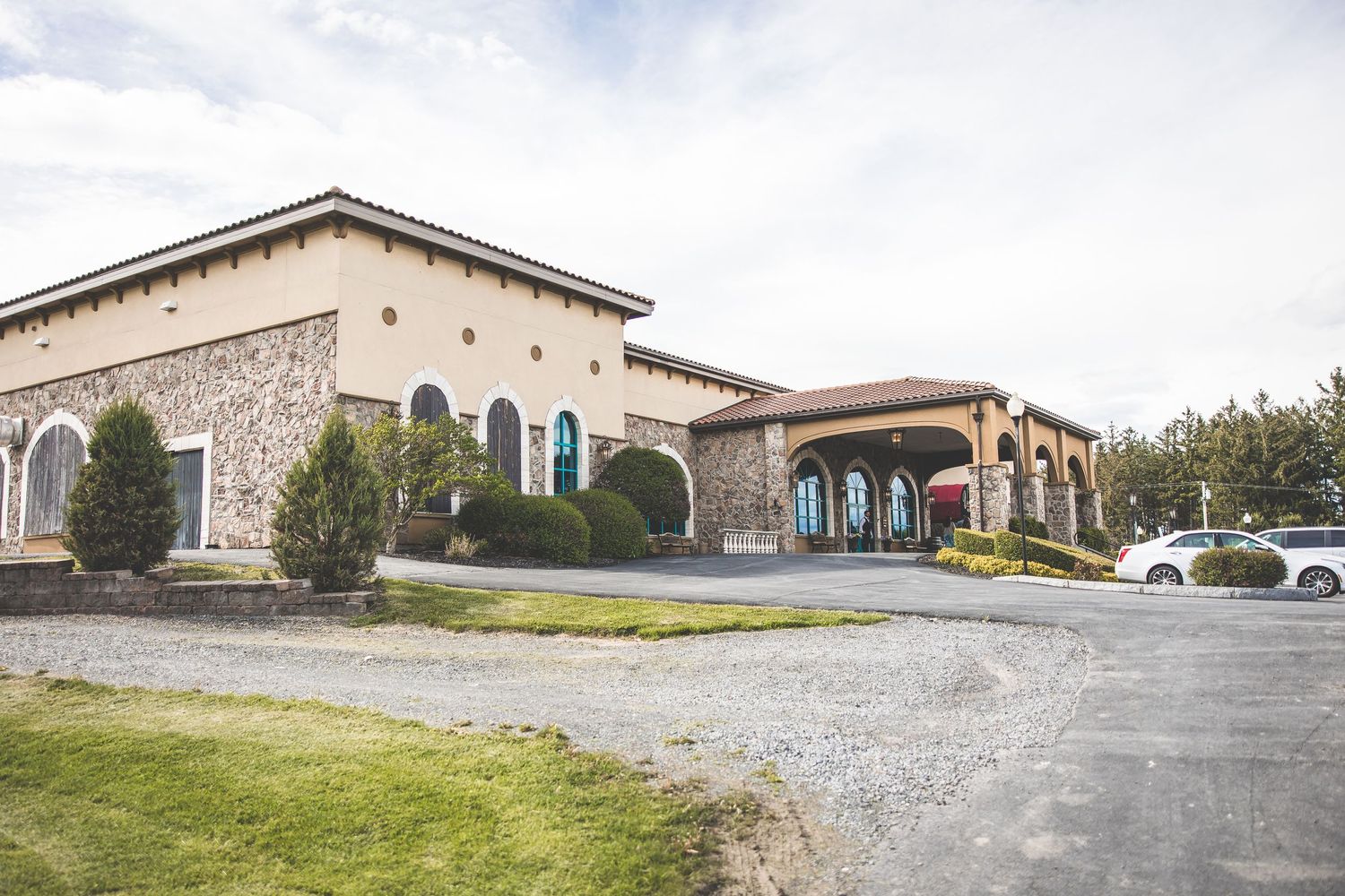 Exterior view of a stone and stucco winery building with Mediterranean architecture style and gravel parking area.