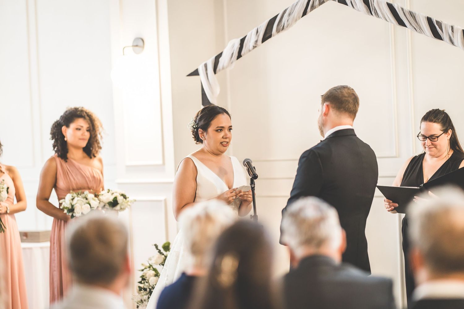 Wedding ceremony in progress with guests watching from rows of chairs in bright venue.