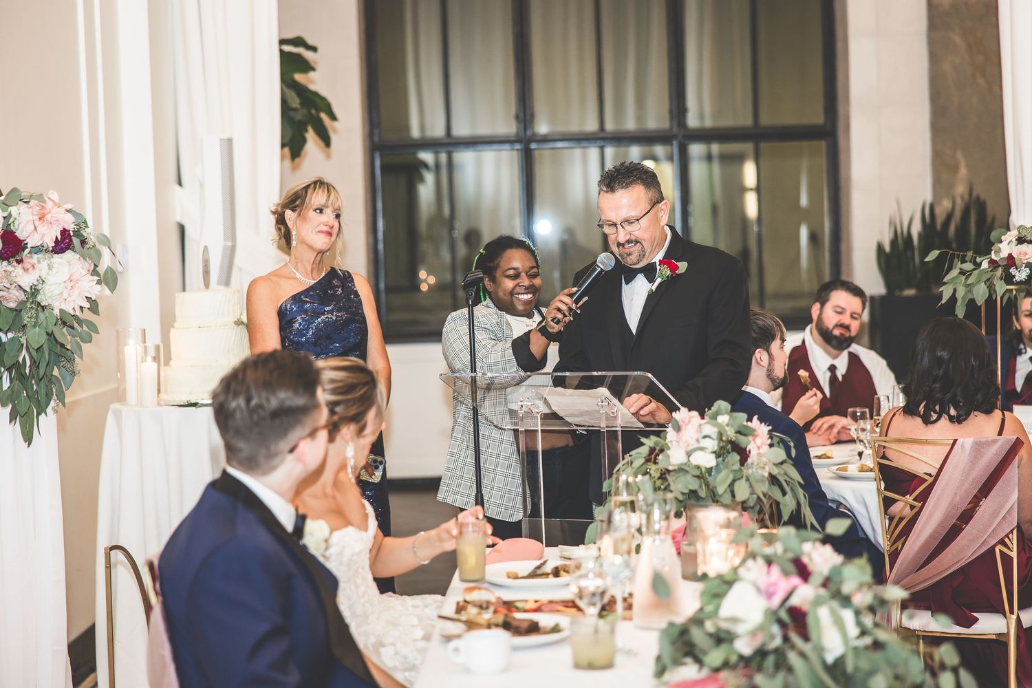 Guests enjoying dinner at an elegant wedding reception with floral decorations and ambient lighting.