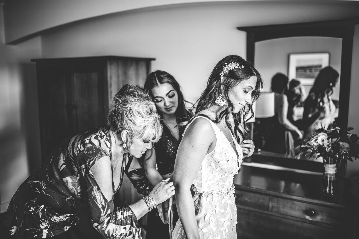 Black and white candid moment of wedding preparation showing emotional support and joy.