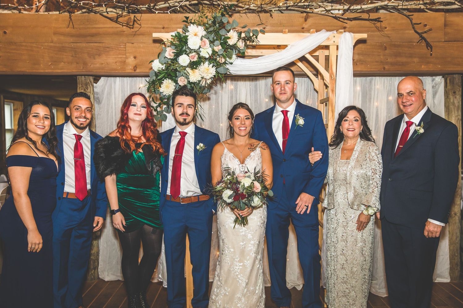 Wedding party in navy suits and formal attire posing together in a rustic indoor venue.