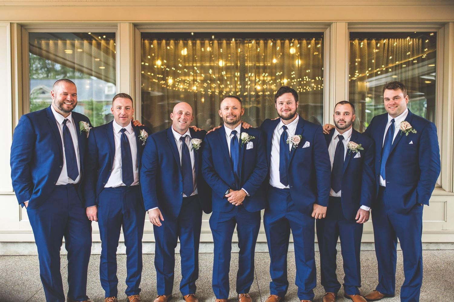 Groomsmen in navy blue suits pose together on brick building porch.