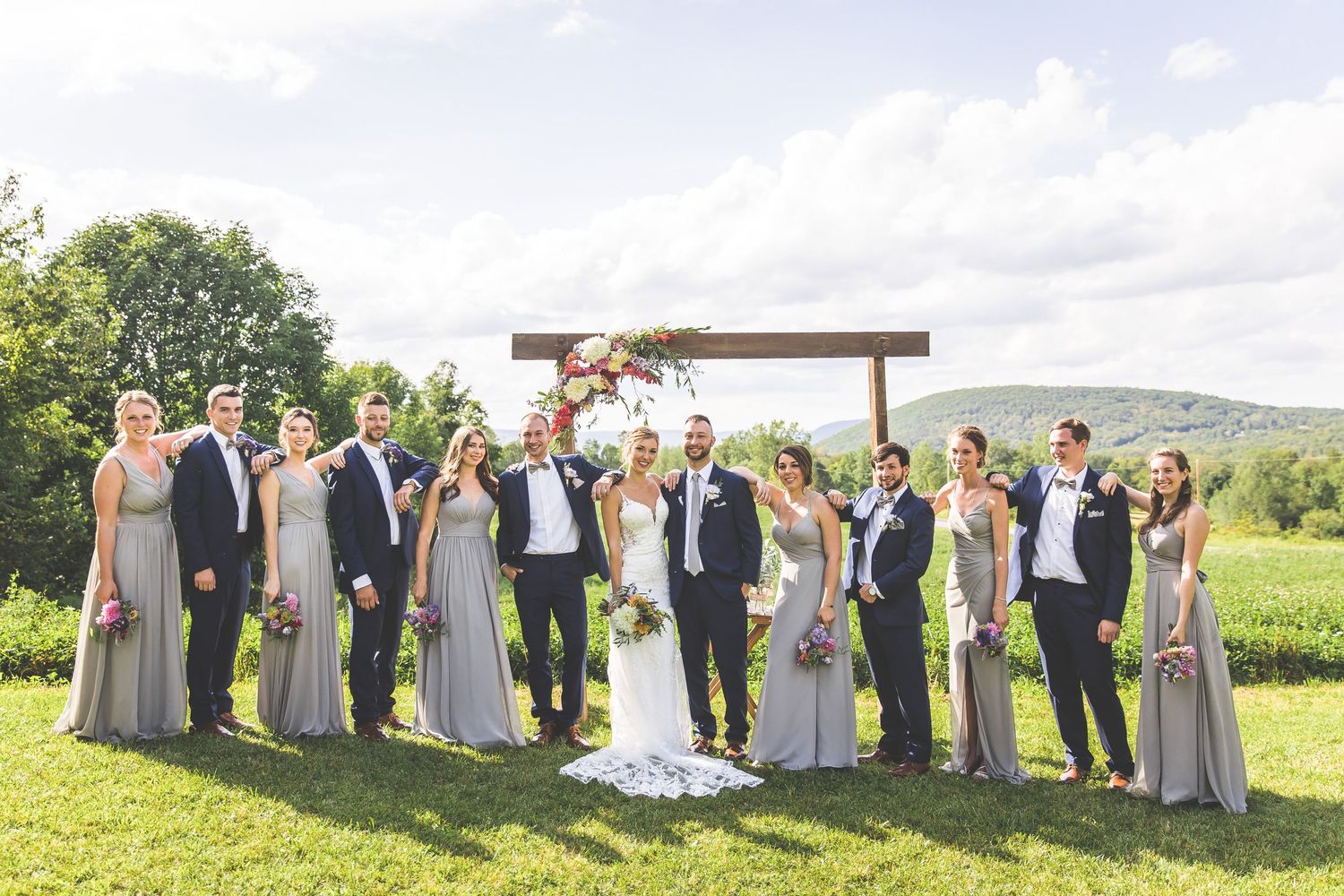 Full wedding party lineup with bridesmaids and groomsmen on scenic hillside.