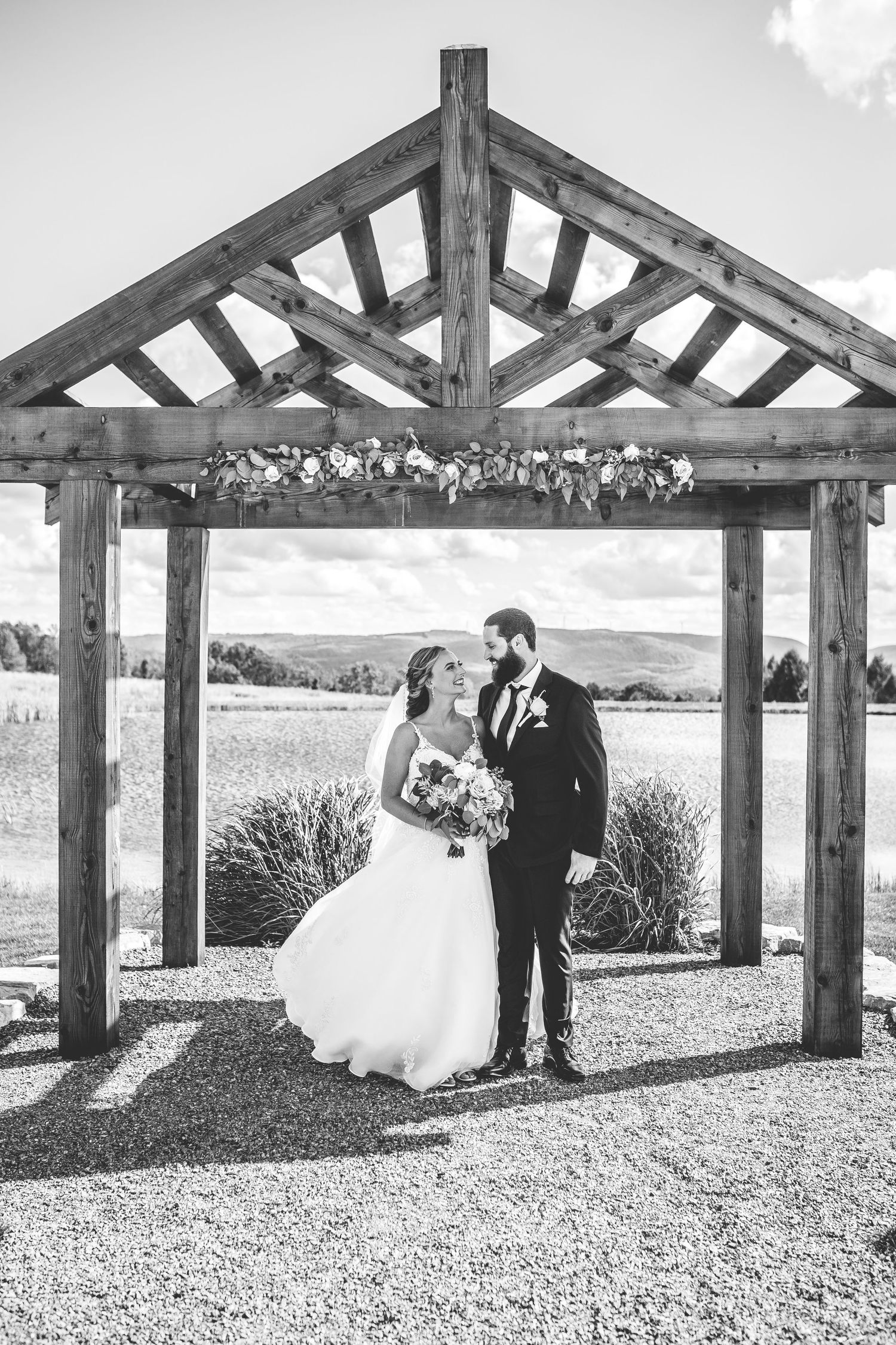 A black and white wedding photo under a wooden pergola decorated with flowers.