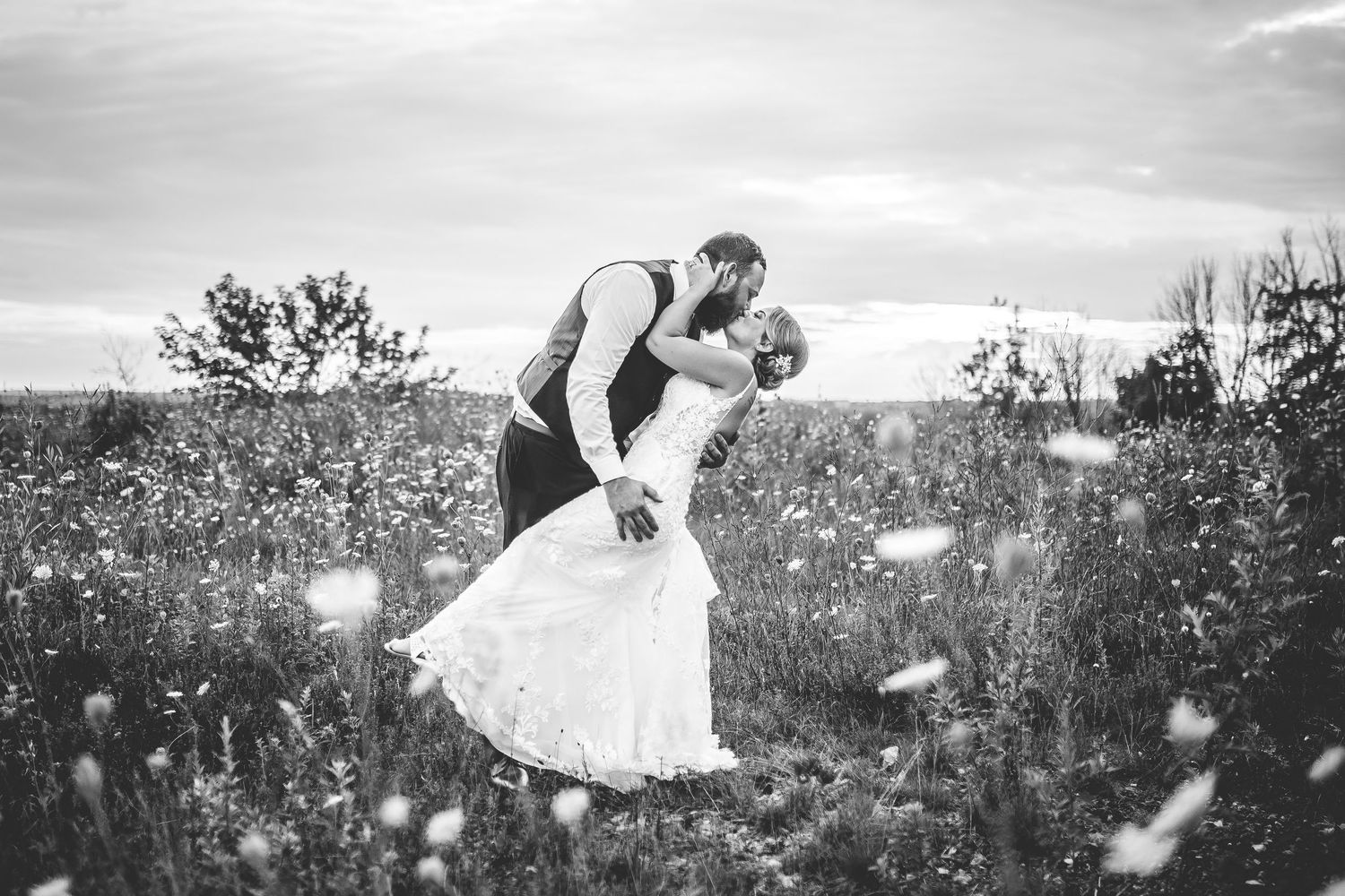 Couple dances playfully through a meadow with flowers at dusk.