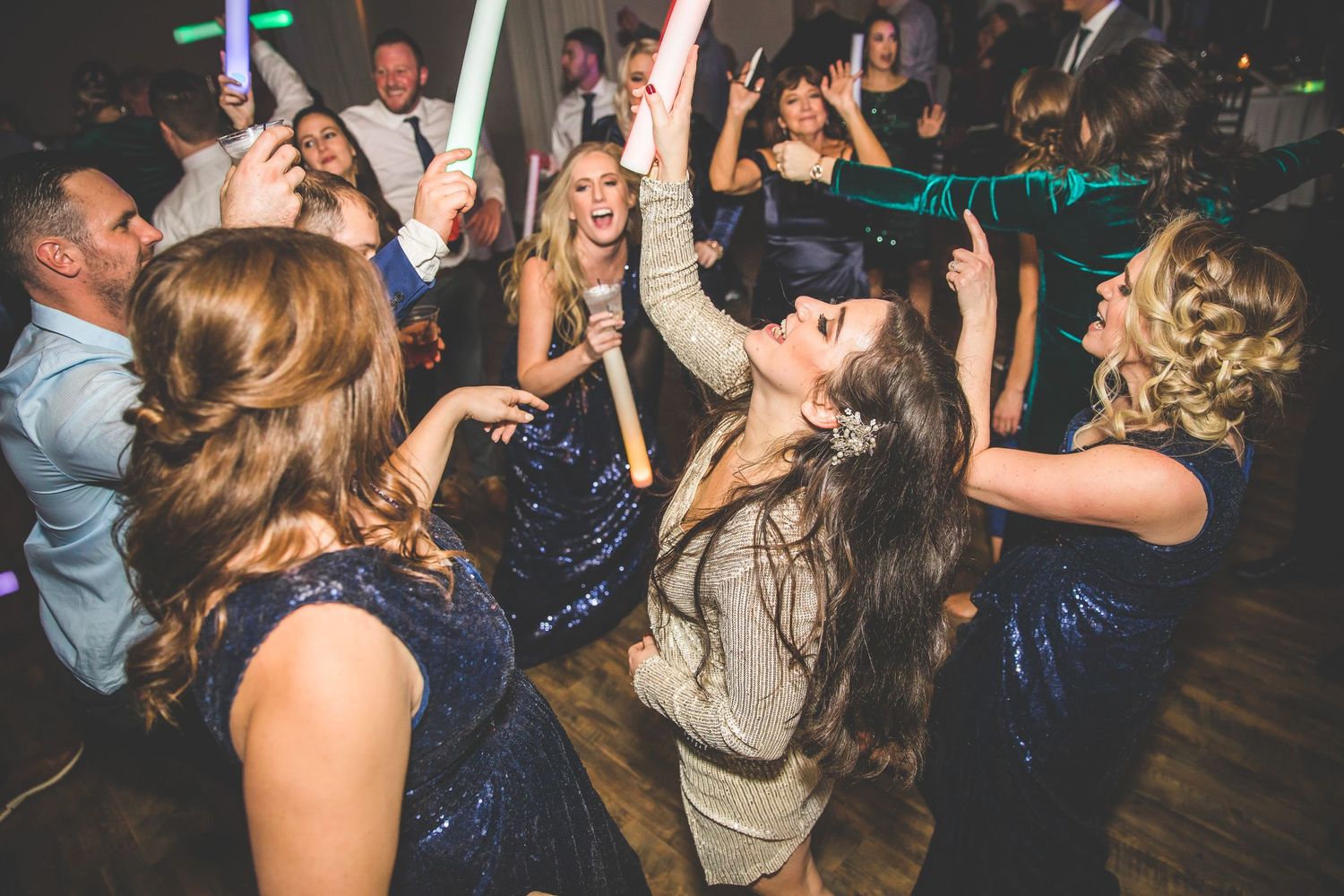 Energetic wedding reception with guests dancing and holding light-up party accessories.