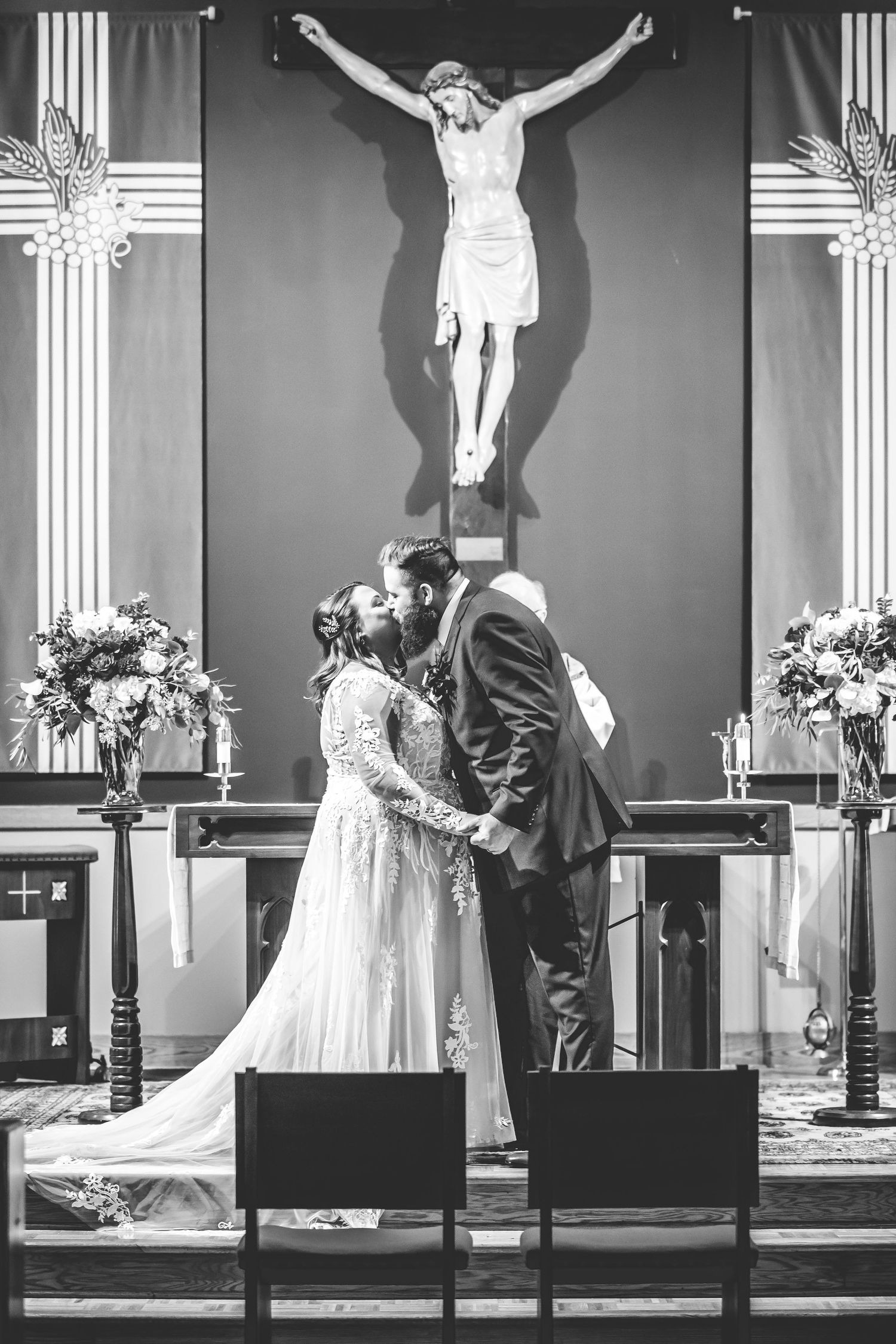 Black and white photo of a church wedding ceremony with a crucifix and floral arrangements.
