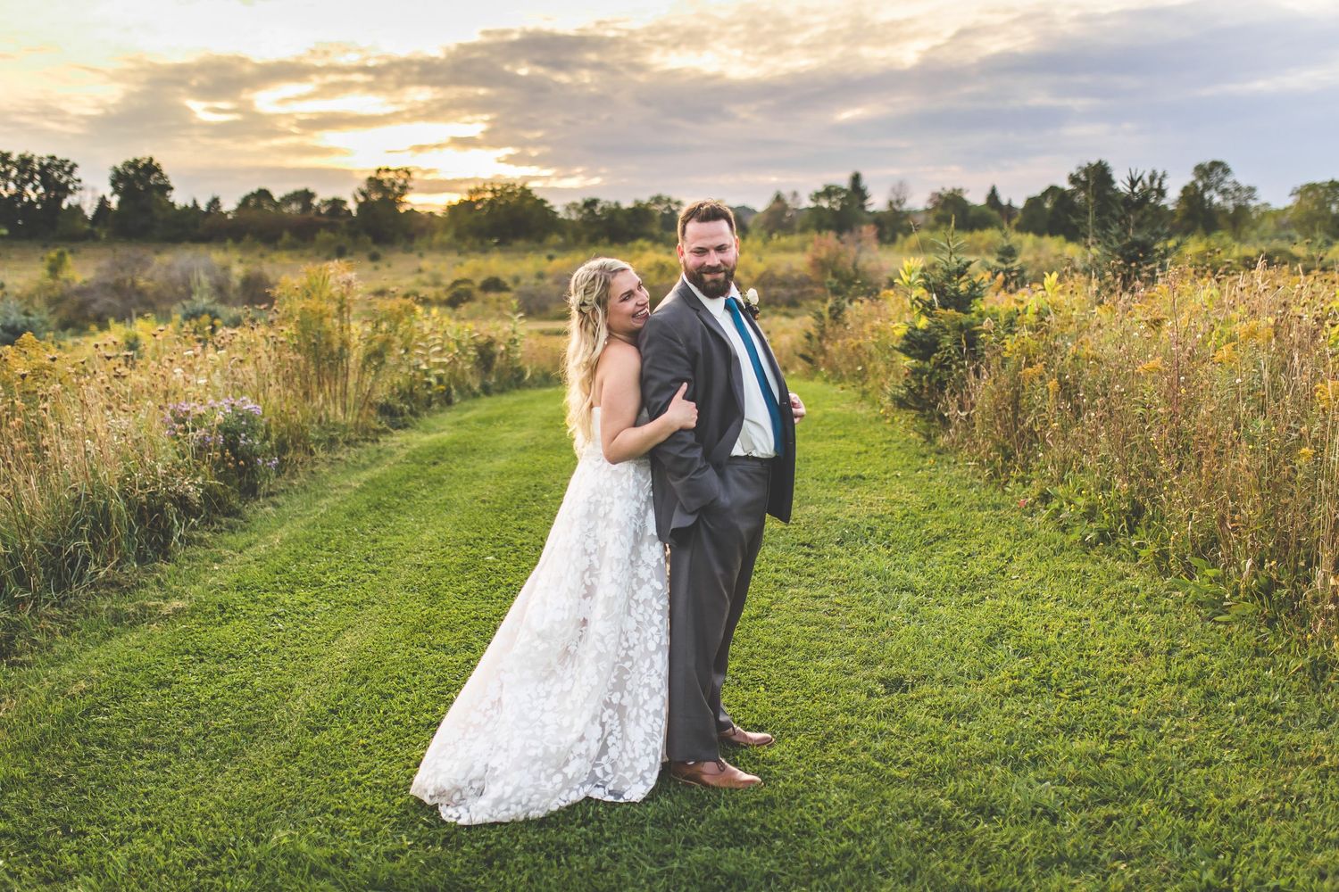 Couple poses in golden field at sunset for romantic wedding photos.