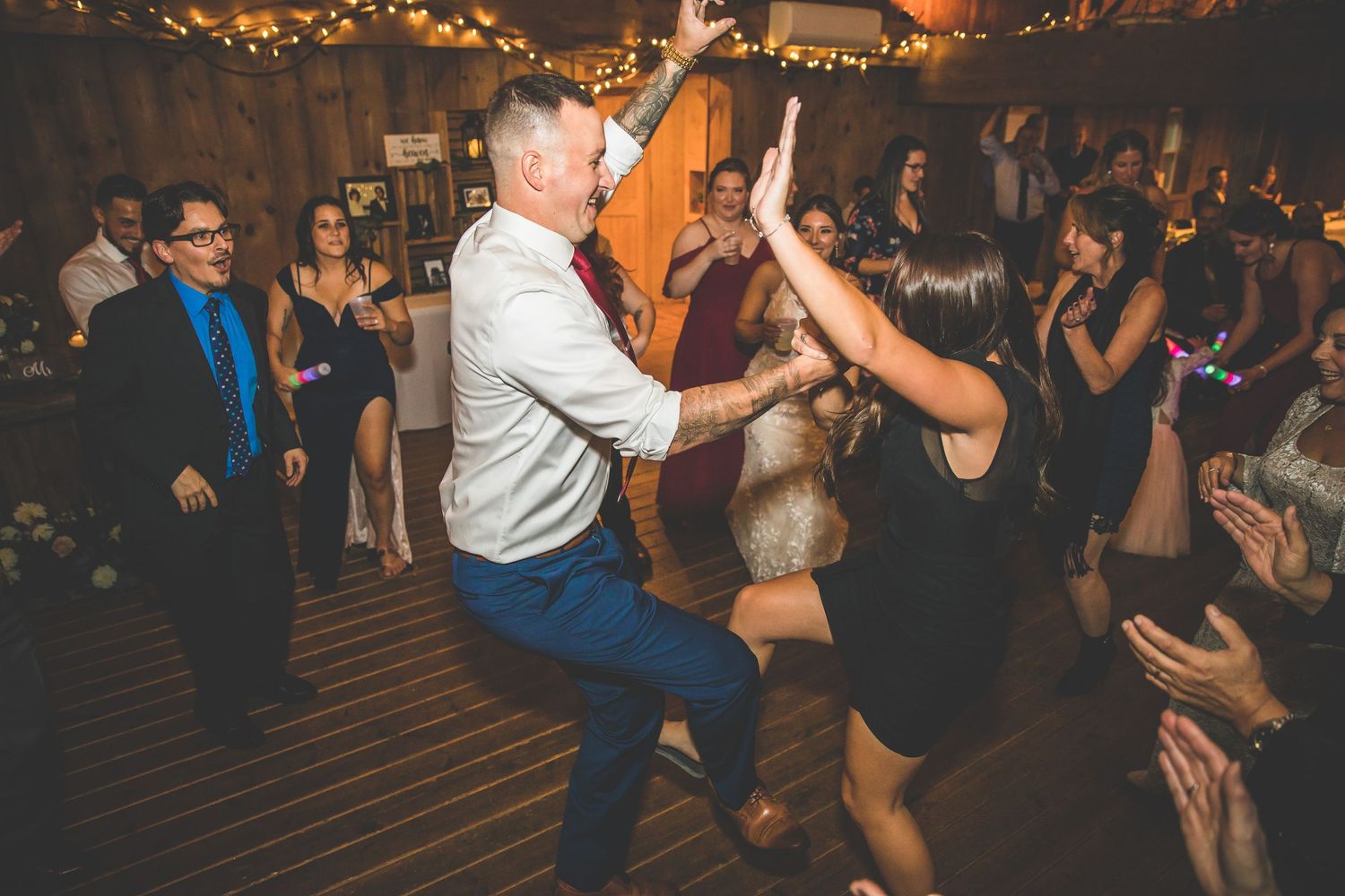 Wedding guests dancing energetically on a dark wooden dance floor at a reception party.