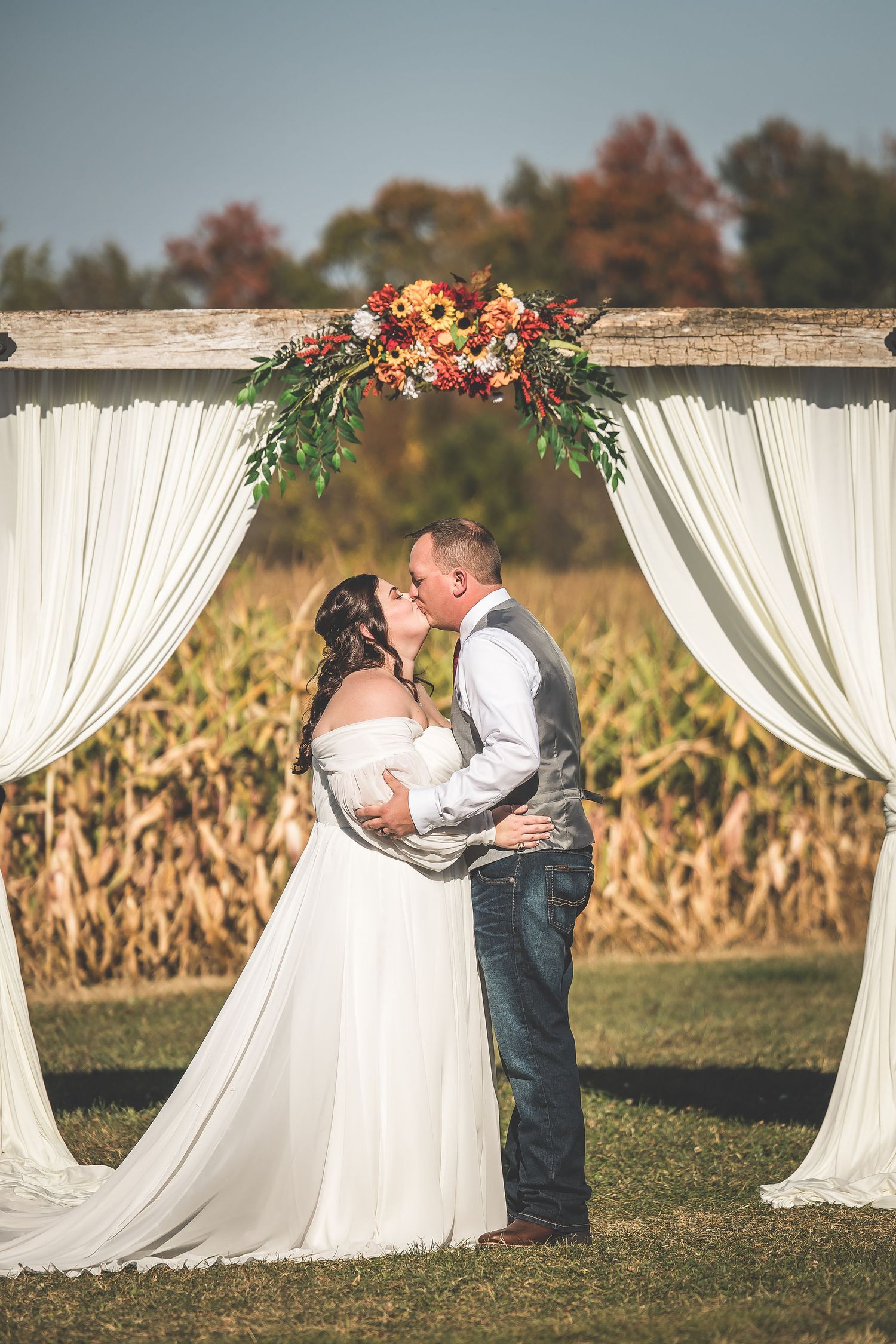 Romantic wedding moment captured at sunset with white draped pavilion and cornfield scenery.