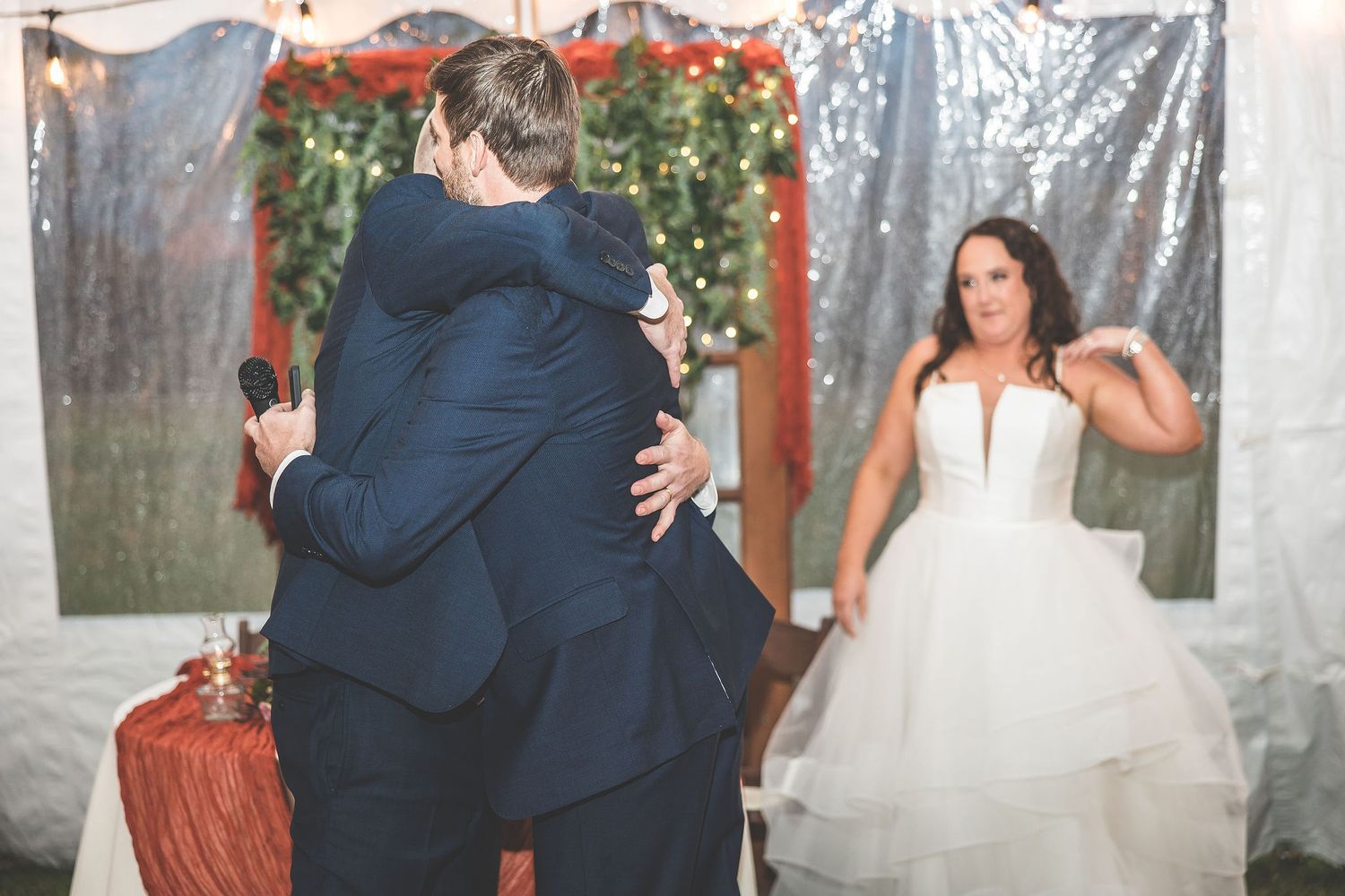 Wedding celebration in outdoor tent with white drapes and burgundy decor elements.