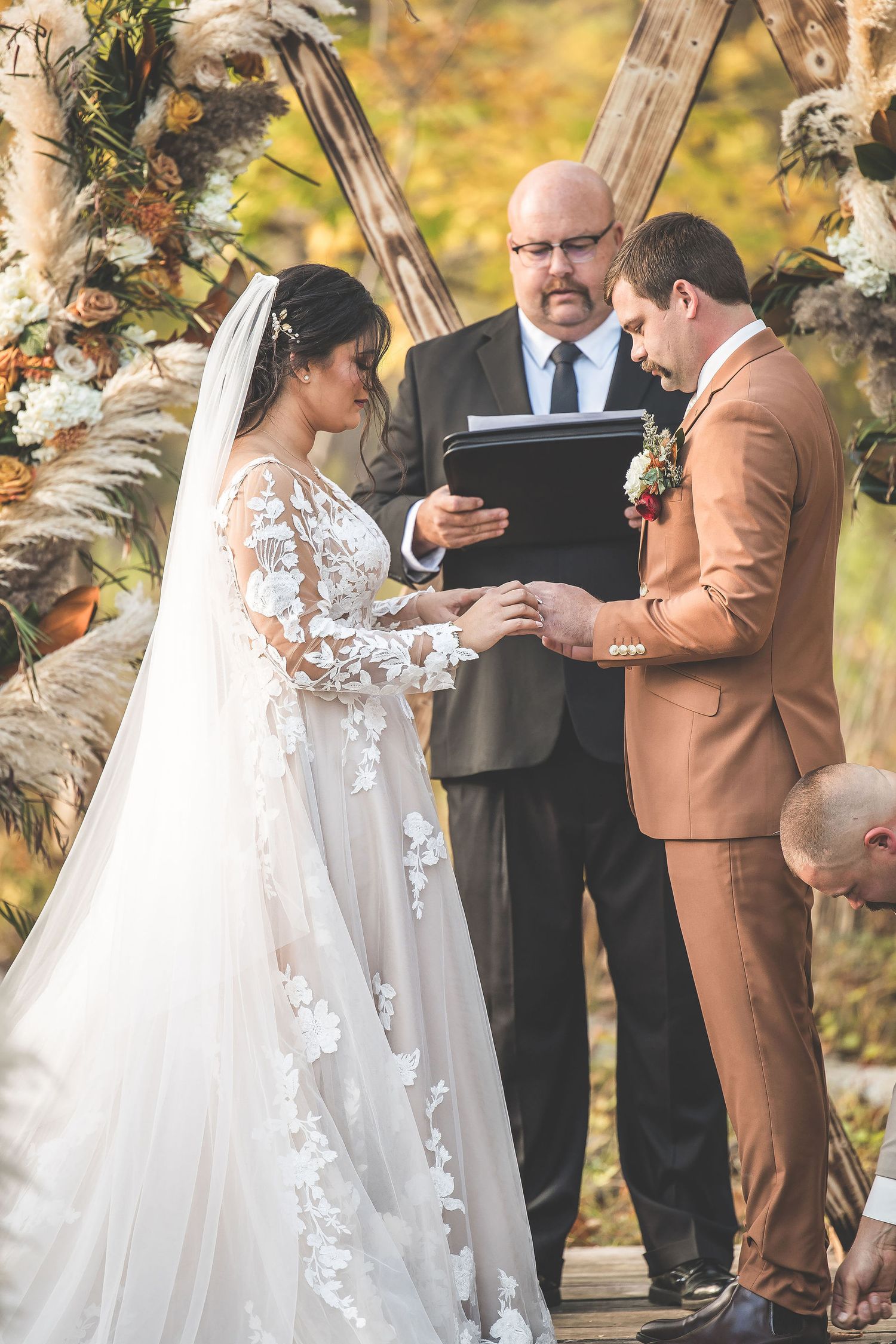 Outdoor autumn wedding ceremony with officiant and couple standing beneath floral arch.