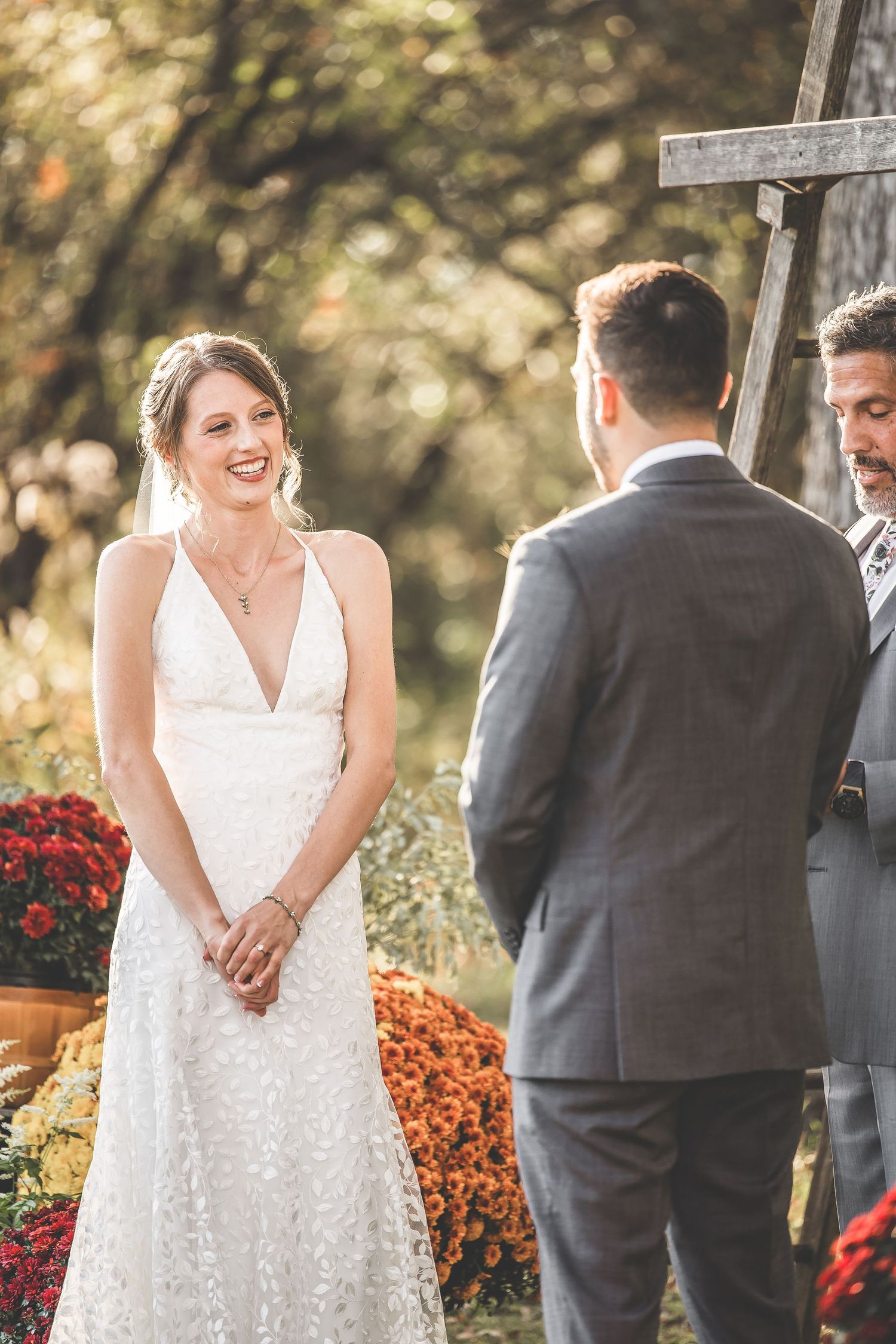 Couple exchanging vows under wooden cross arch with fall flowers and autumn decor.