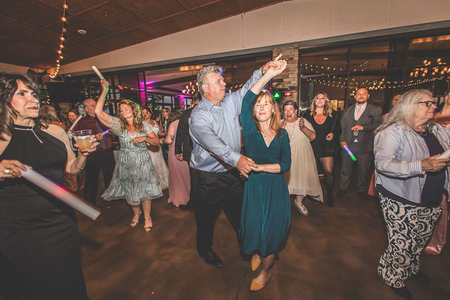 Wedding reception dance floor panorama showing guests celebrating under string lights.