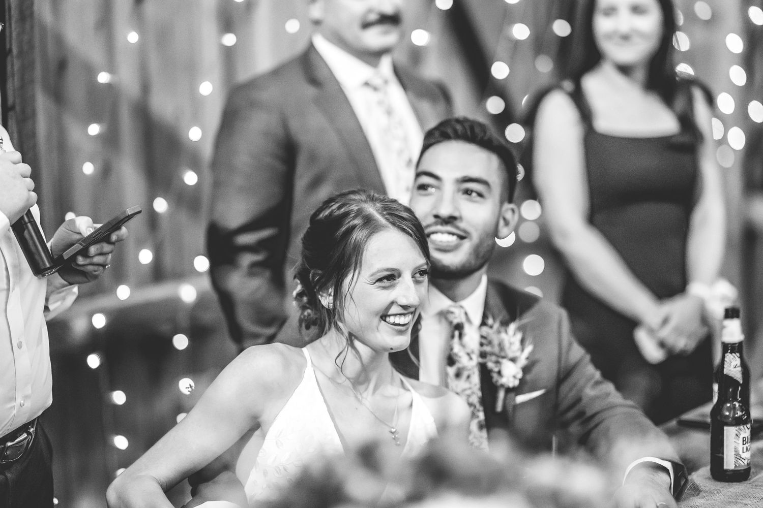 Black and white photo of wedding reception guests celebrating with string lights in background.