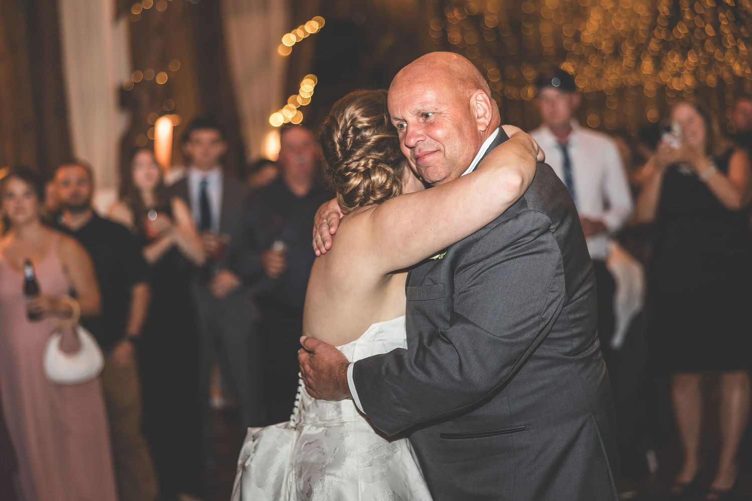 Emotional dance moment at wedding reception with guests watching in background.