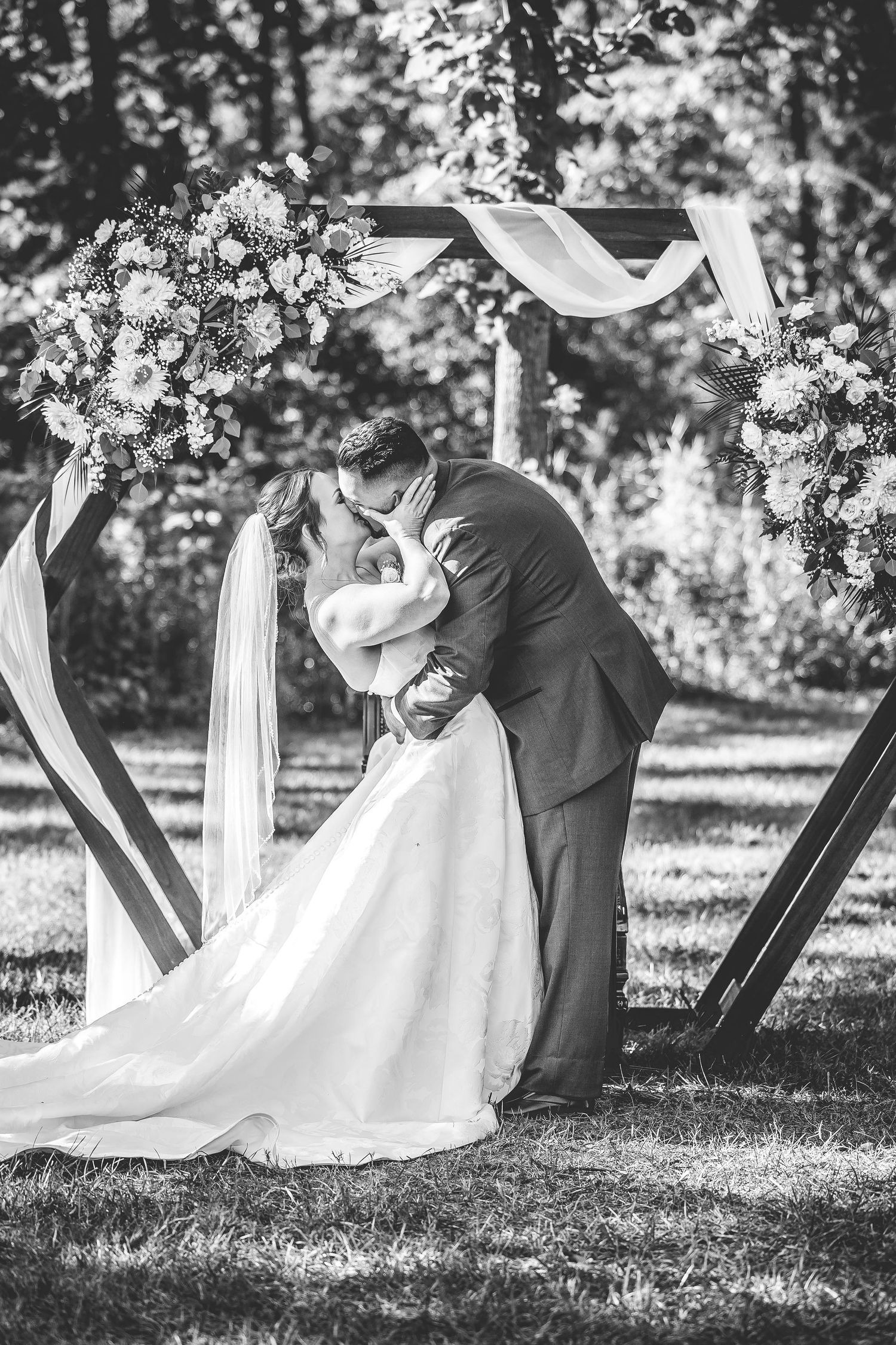 Black and white photo of a romantic wedding ceremony moment under a decorated arch.