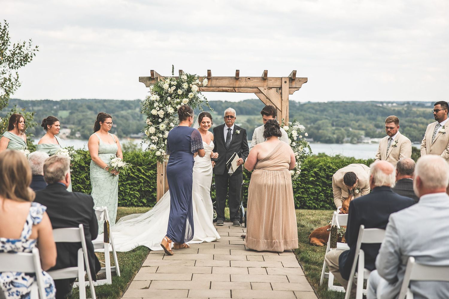Outdoor wedding ceremony with wooden pergola and sage green bridesmaid dresses.