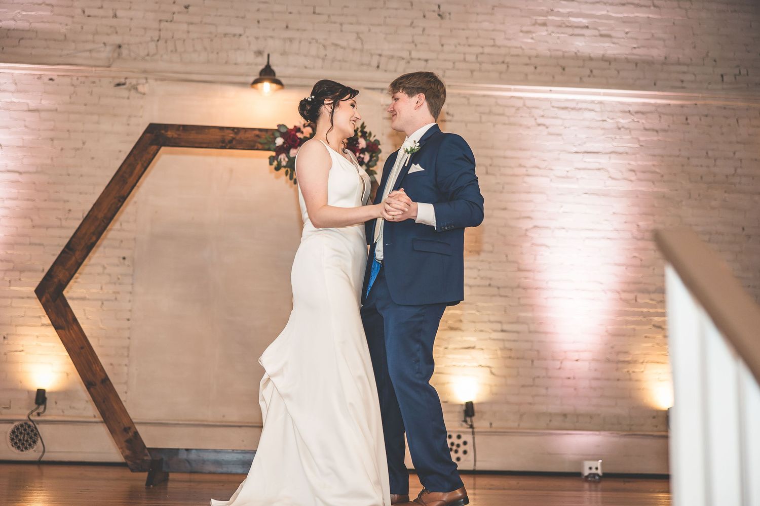 Romantic dance moment captured in a beautifully lit brick-walled reception space.