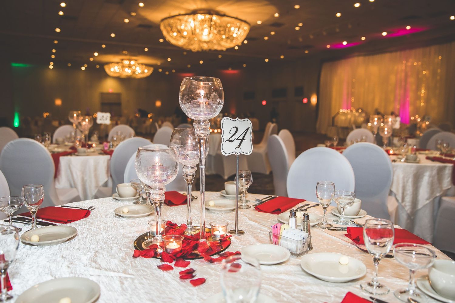 Reception tables decorated with red accents and elegant place settings under warm chandelier lighting.