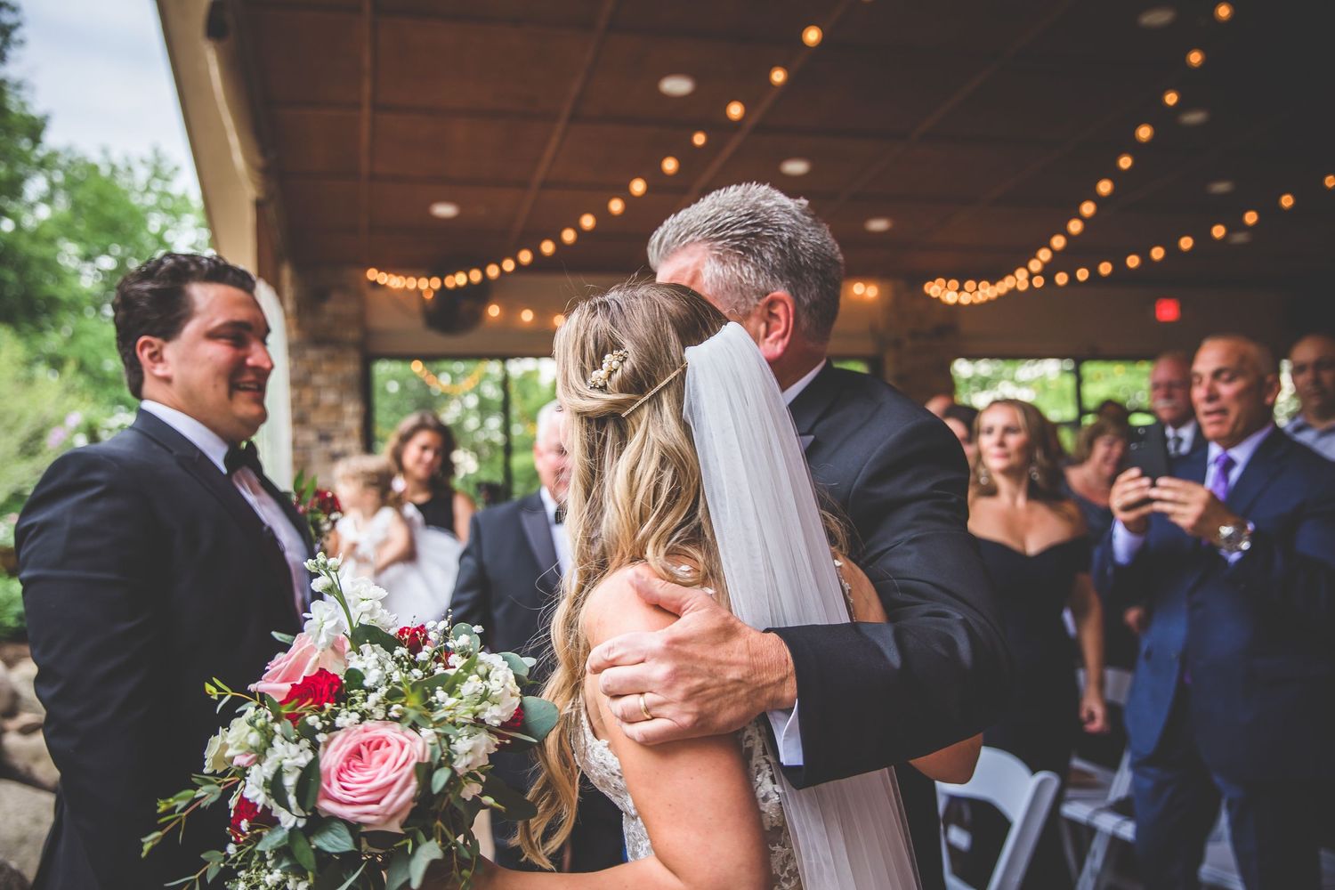 Wedding ceremony in progress under string lights with guests seated in rows.