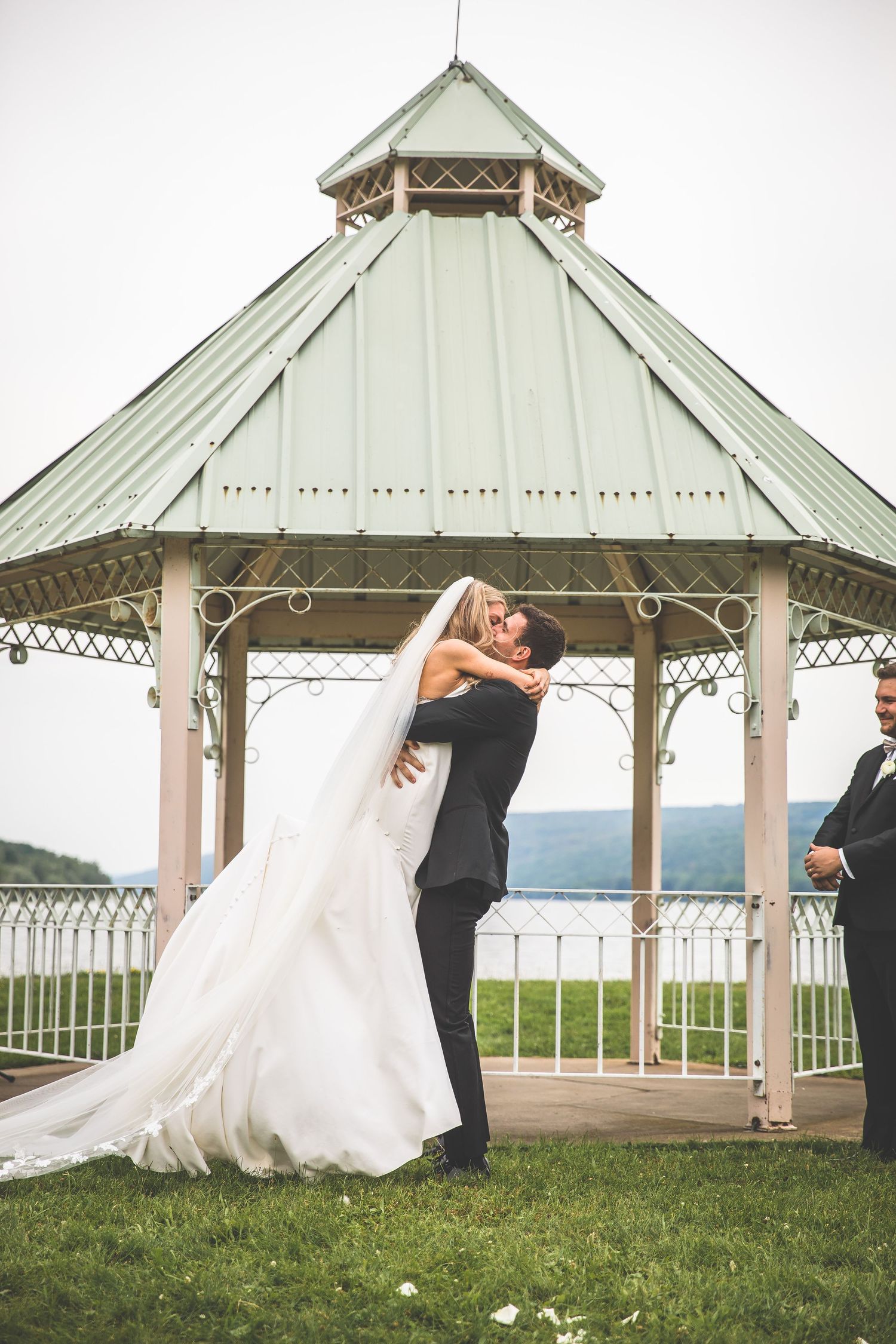 Romantic wedding moment captured under white gazebo with scenic mountain backdrop.