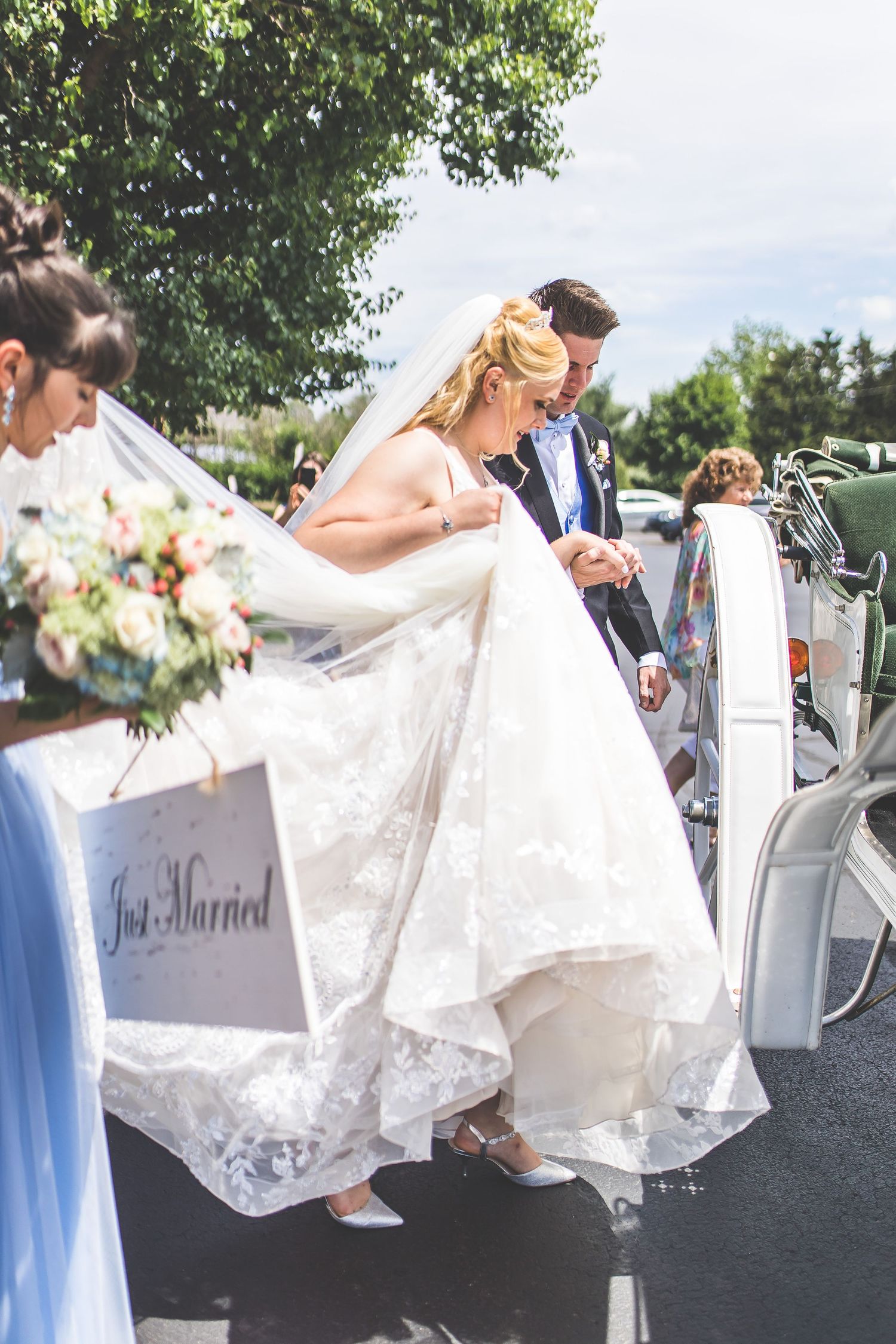 Elegant white wedding dress billows in breeze as couple boards decorative carriage.