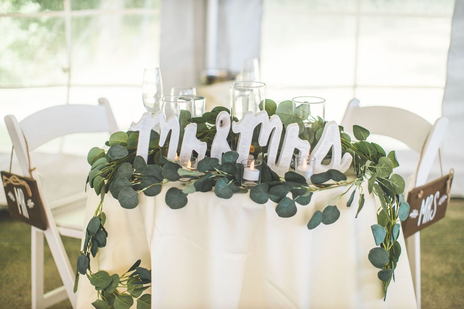 Wedding reception tables decorated with eucalyptus garlands and white linens.