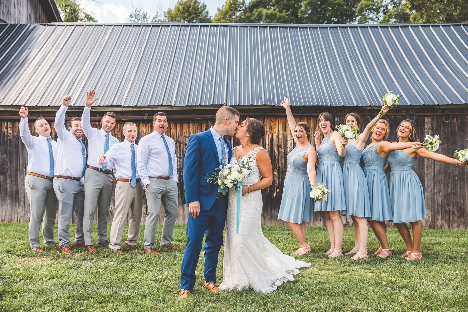 Wedding party celebrates with the newlyweds in front of a rustic barn.