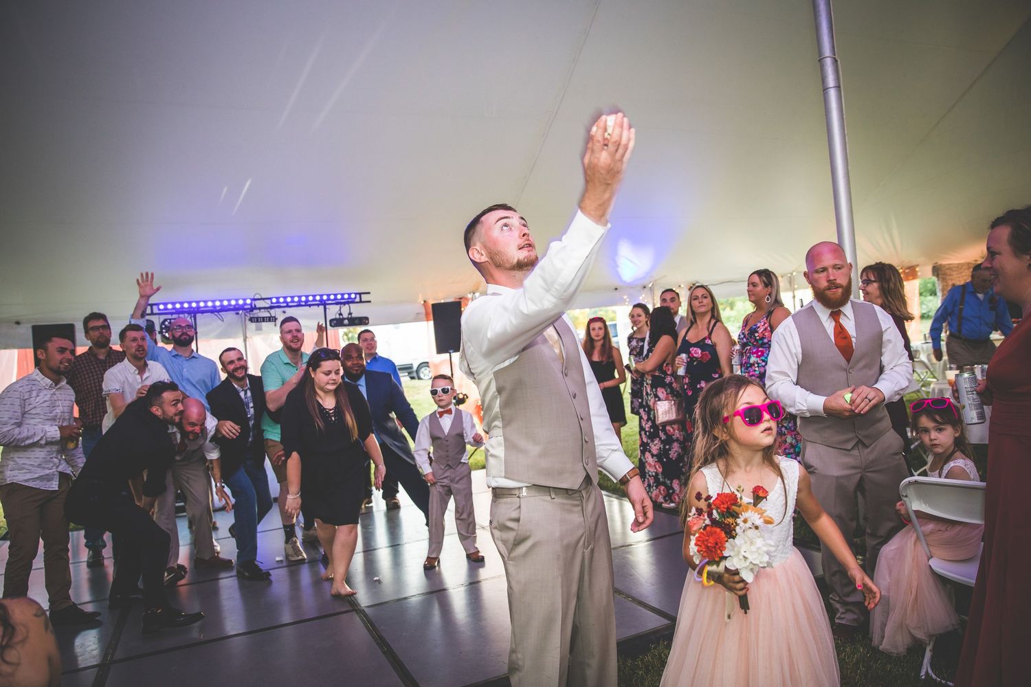 Wedding guests dancing and celebrating at a lively reception with blue lighting and a festive atmosphere.