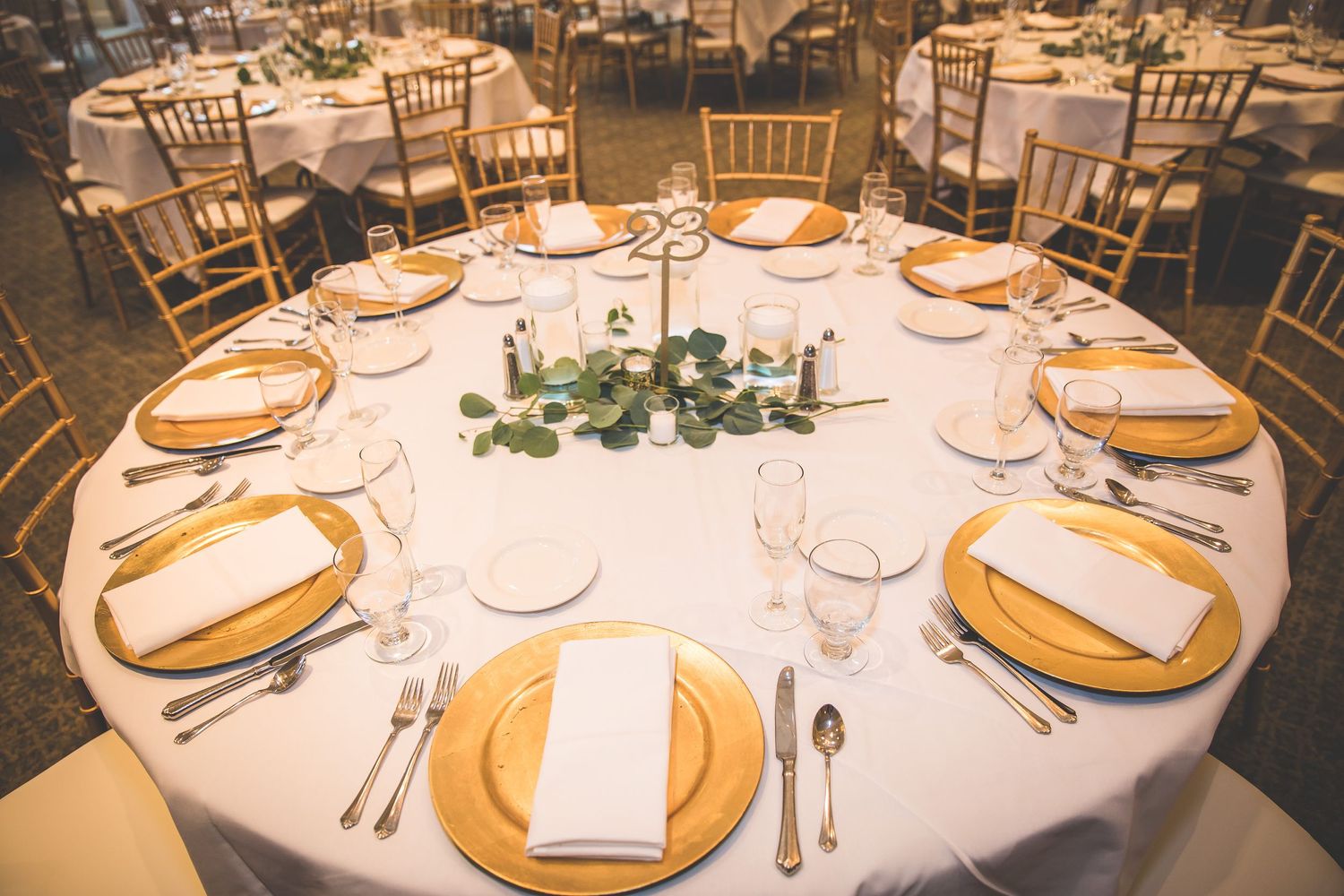 Elegant wedding reception tables set with gold chargers, white linens and floral centerpieces.