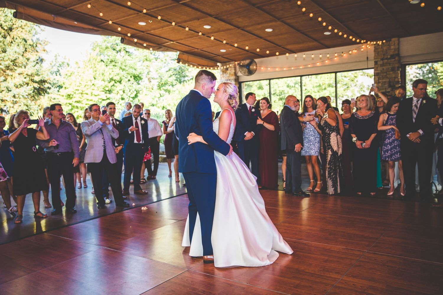 Wedding reception dance floor with string lights overhead and guests watching first dance.