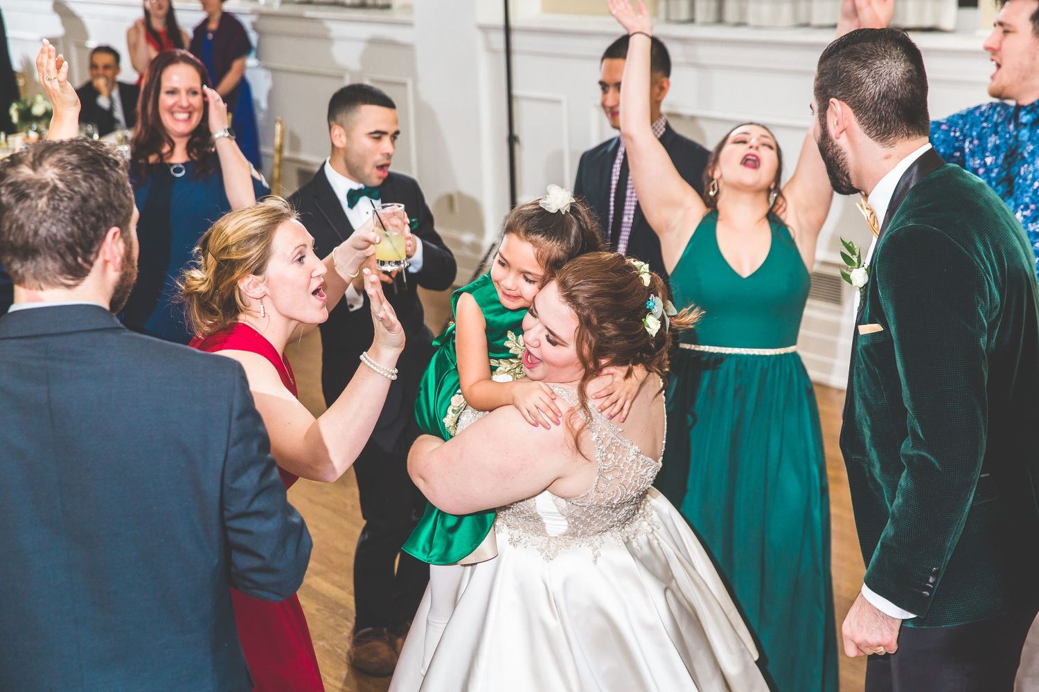 Wedding guests in formal attire dance and celebrate in an elegant ballroom with emerald green accents.