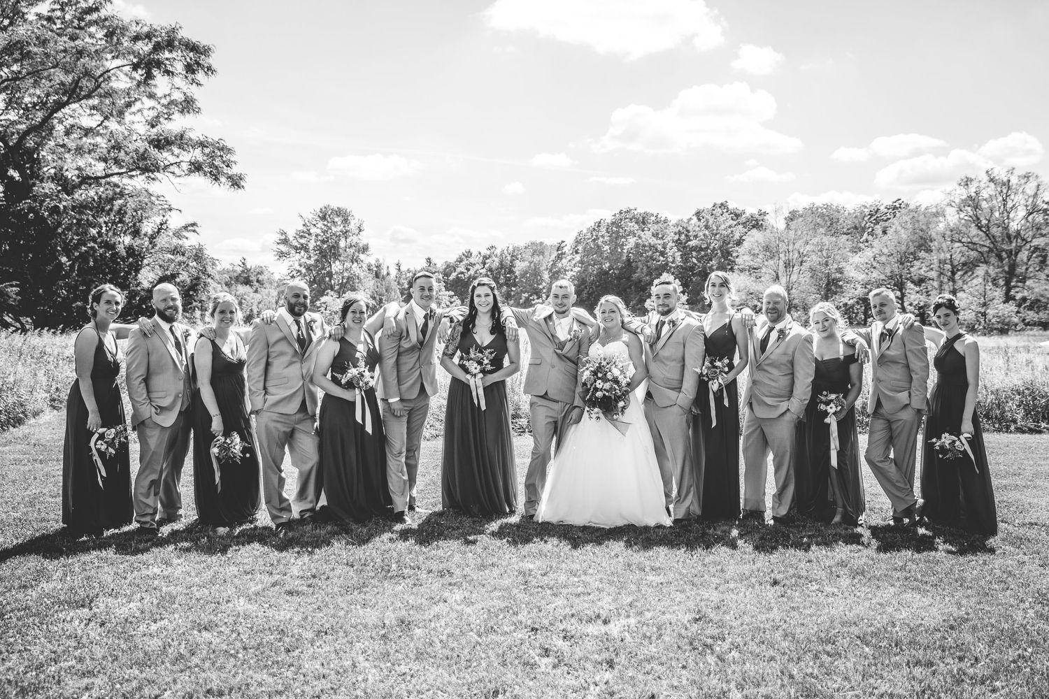 Large wedding party poses together outdoors in black and white photography.