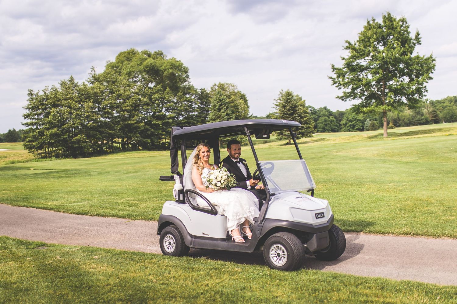 Wedding party riding in white golf carts across a sunny golf course.