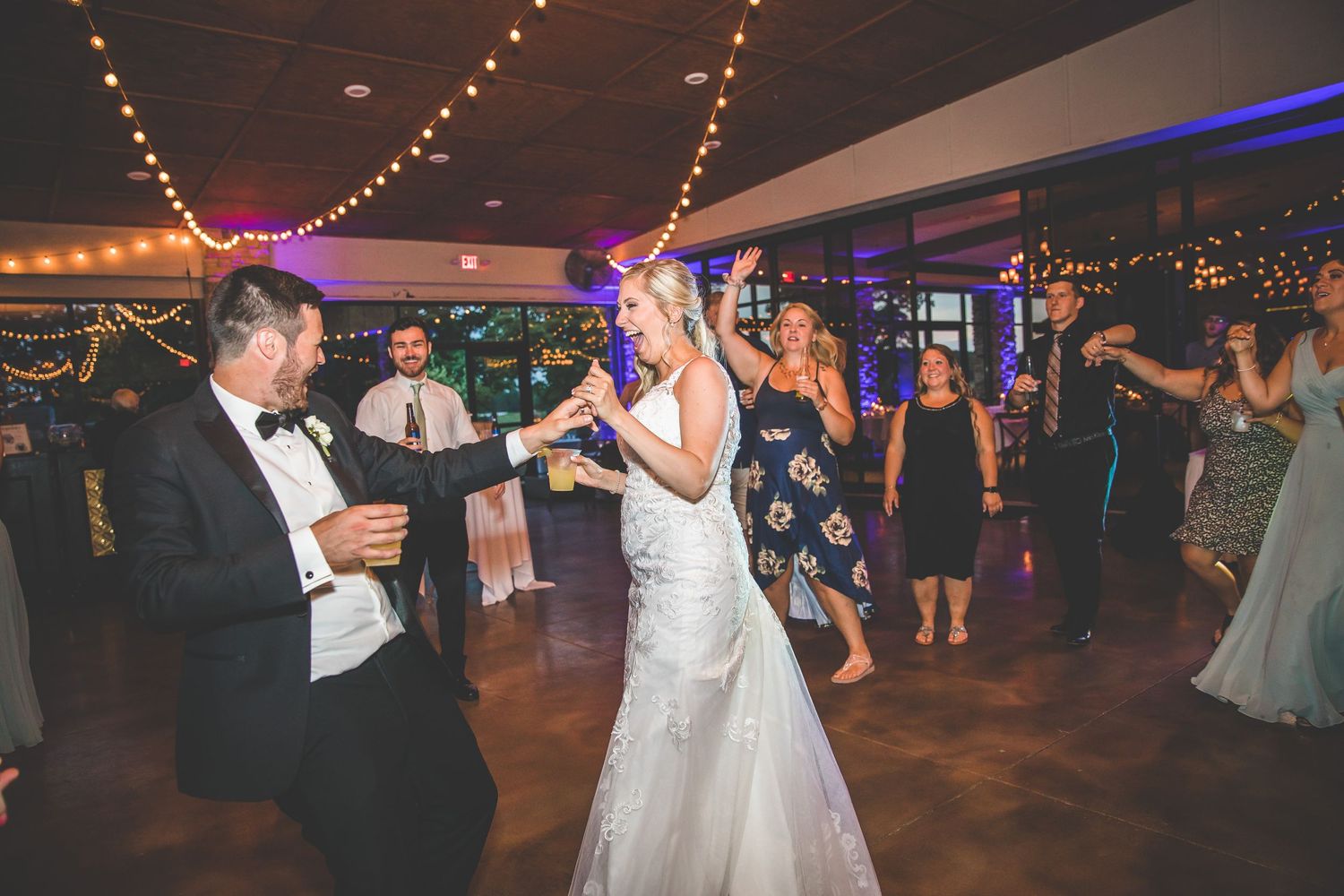 Wedding guests dancing and celebrating on a dimly lit dance floor with string lights overhead.