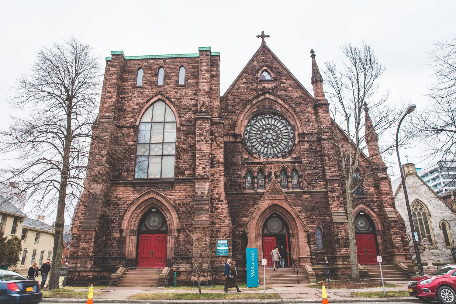 Exterior view of a historic red brick Gothic church with stained glass windows and stone details.