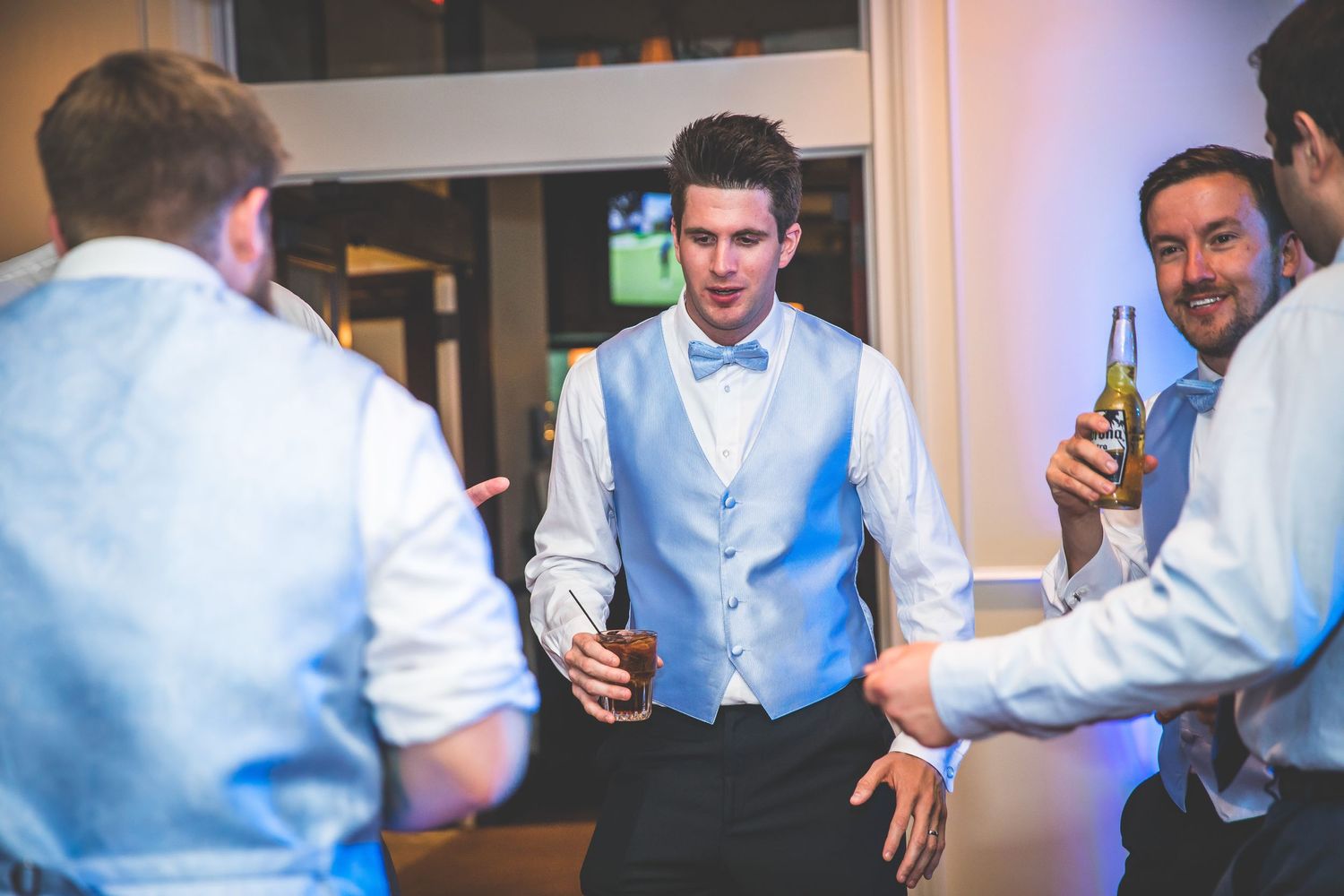 Groomsmen celebrate at a wedding reception with drinks and laughter.