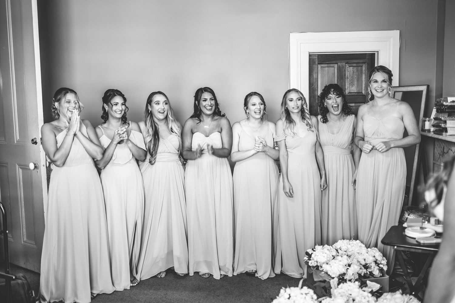 Black and white photo of bridesmaids lined up in matching dresses during wedding preparations.