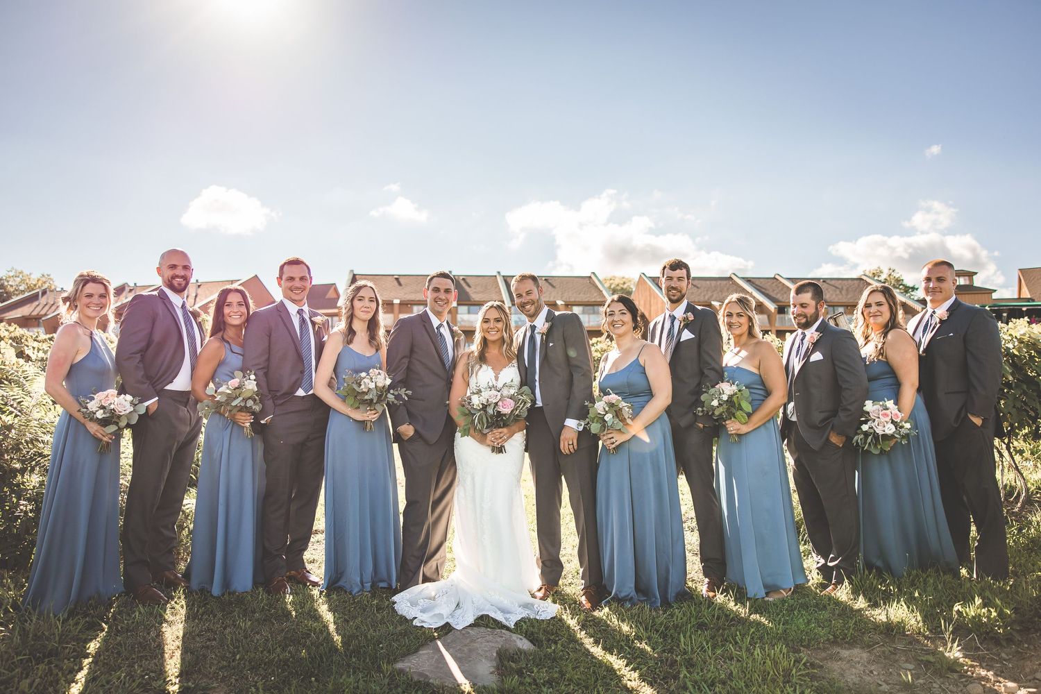 Wide angle shot of entire wedding party gathered on hillside for group photos at vineyard venue.
