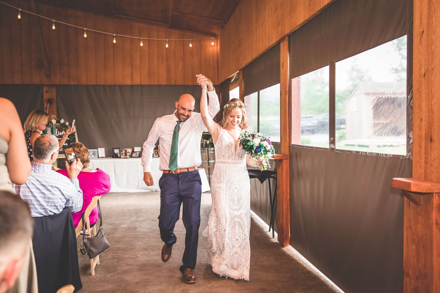 String lights illuminate a rustic wooden barn interior during a wedding reception.