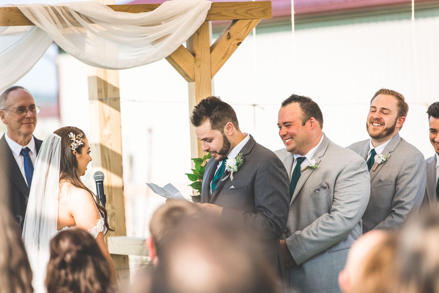 Exchange of rings during outdoor wedding ceremony under decorated wooden pergola.