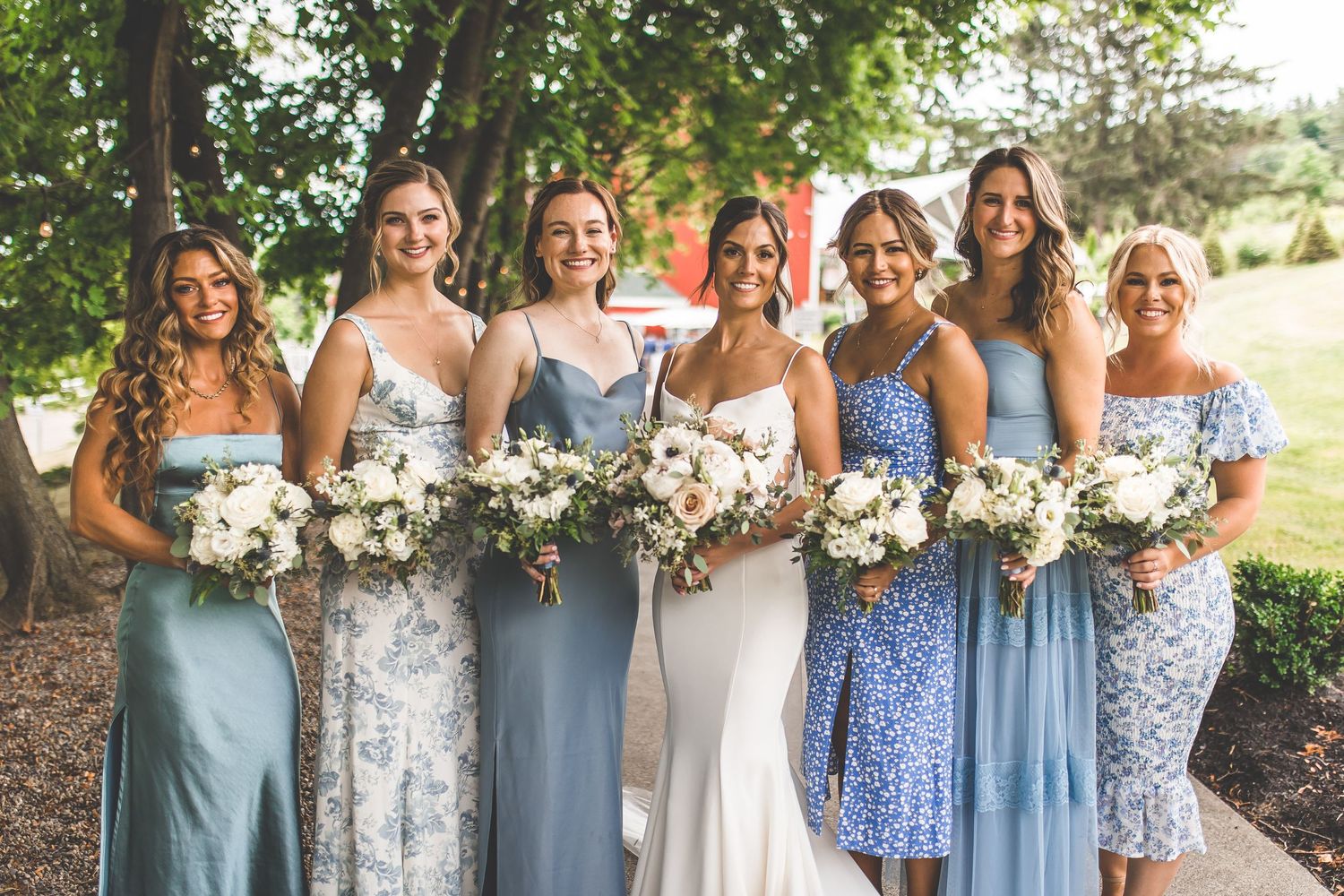 Wedding party in coordinated blue and floral dresses poses together outdoors.