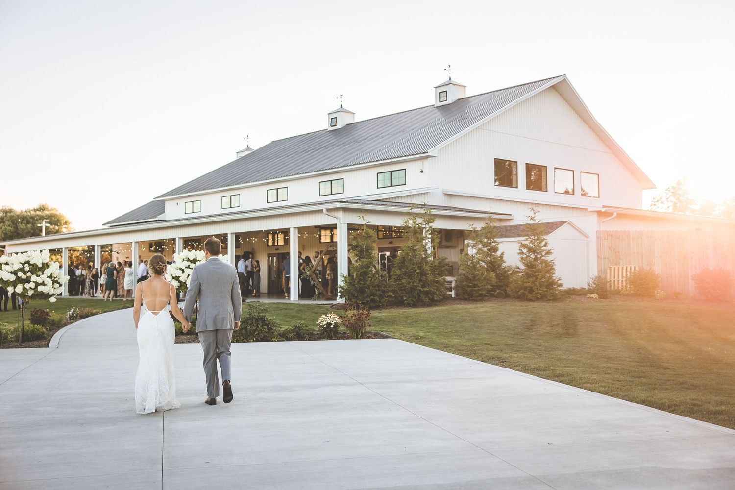 Wedding couple walking towards a white barn venue at sunset.