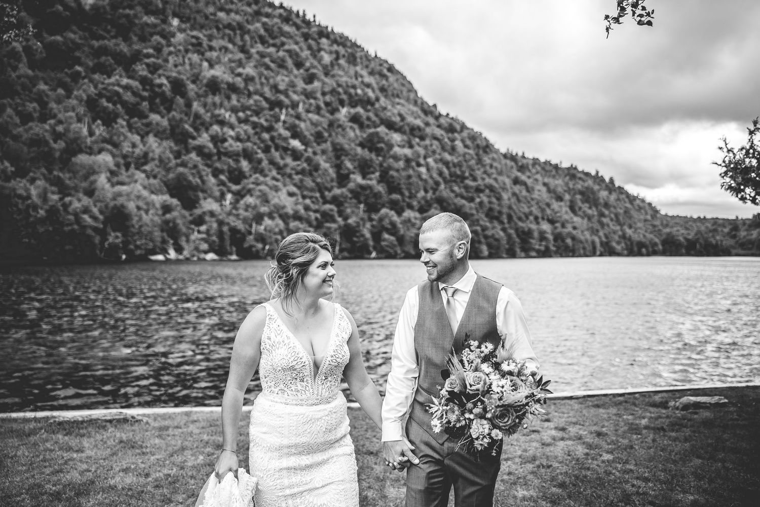 Black and white wedding photo of a couple walking by a scenic mountain lake.