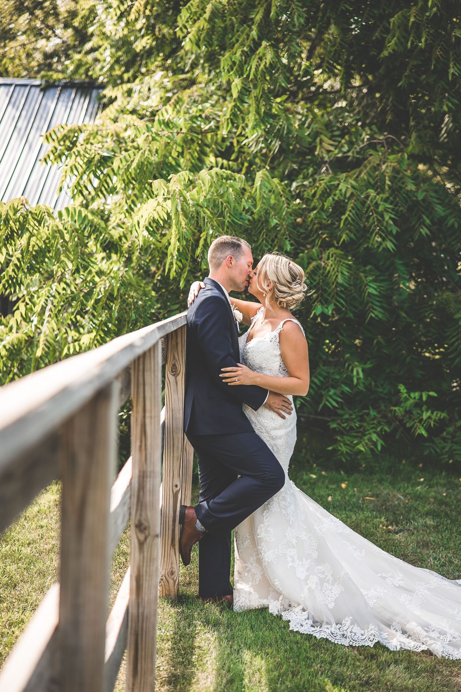 A romantic wedding moment captured on a wooden bridge surrounded by lush summer foliage.