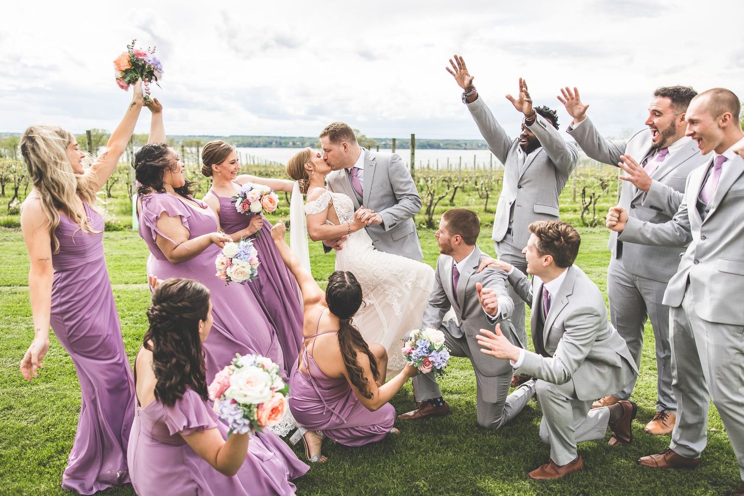 Energetic wedding party jumping and celebrating together in a vineyard.