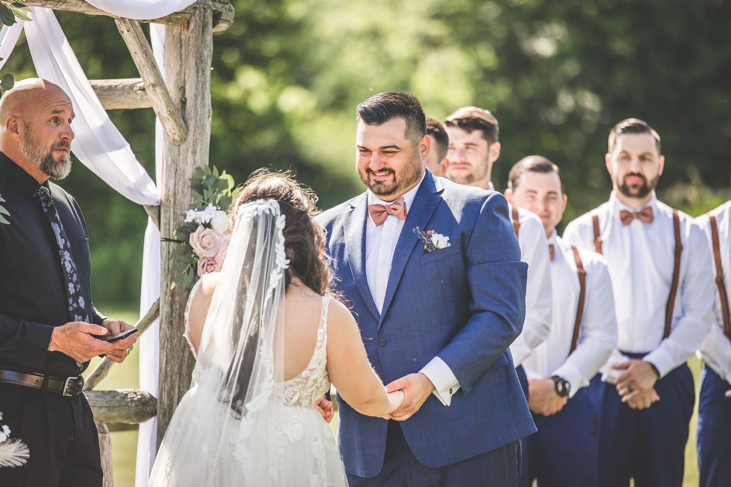 Wedding ceremony participants gather under a wooden arch during an outdoor celebration.