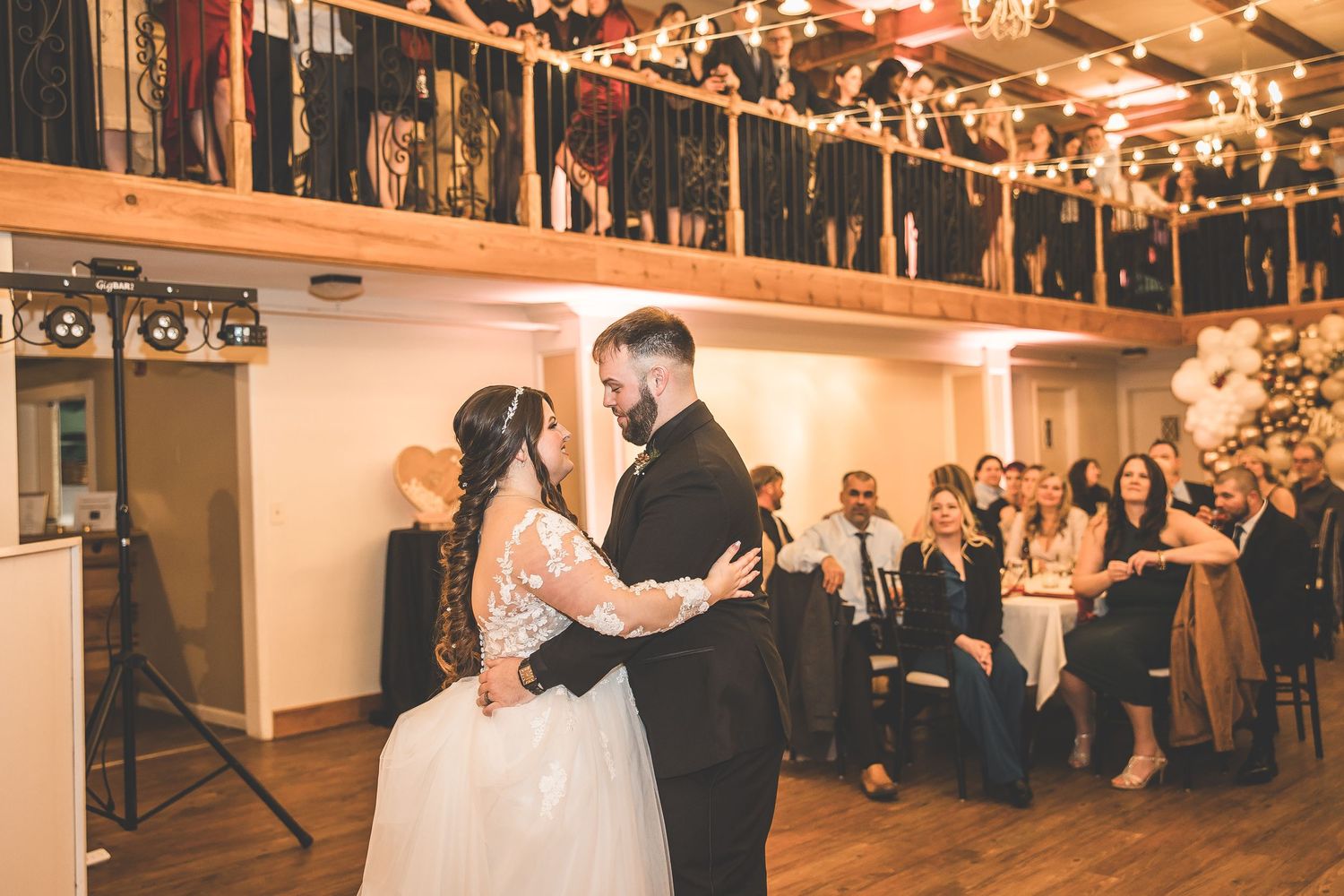 Wedding reception dance floor scene with string lights and guests in the background.